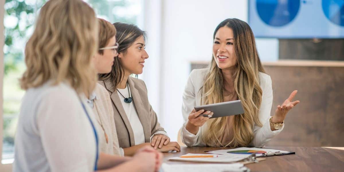 woman holding ipad talking to 3 other ladies 