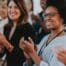 A diverse group of professionals smiling and applauding during a workplace event or presentation, conveying appreciation, recognition, and positive company culture.