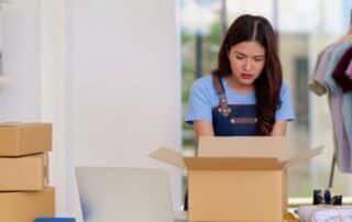 Concerned online store owner looking into a returned package with frustration, surrounded by shipping boxes and merchandise.